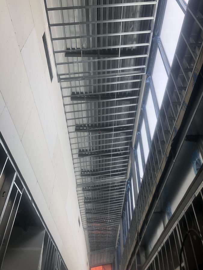 Looking up at a long run of steel ceiling framing beside high clerestory windows